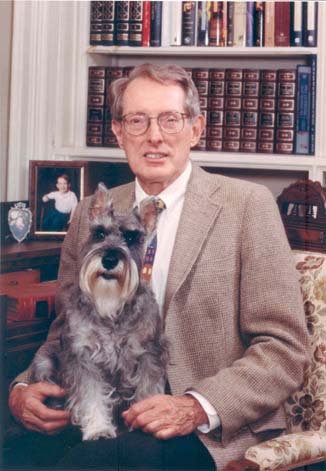 Joseph F. Shubert posing in front of books with a small gray dog on his lap