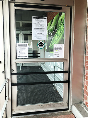 Entrance door to a supermarket, with a signs about policies in place because of the COVID-19 pandemic.