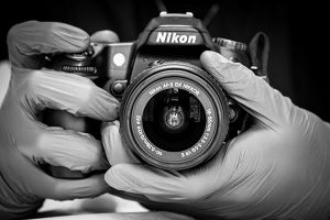 black-and-white photo of gloved hands holding a Nikon camera