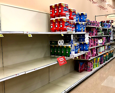 Partly empty grocery shelves, with several packages of toilet paper at the end of the section.