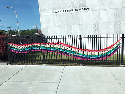 rainbow colored ribbon weaved through fence in front of marble building