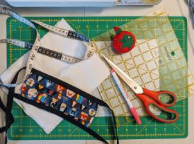 fabric mask, scissors, pin cushion and other sewing supplies on a cutting mat.