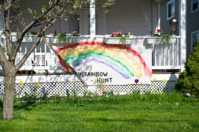 A white porch with a home-made banner over the railing that has a rainbow and the words Rainbow Hunt